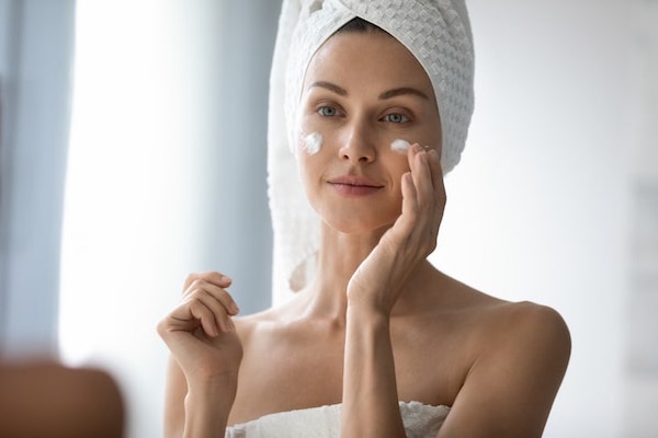 Woman in towel applying moisturizer in front of mirror