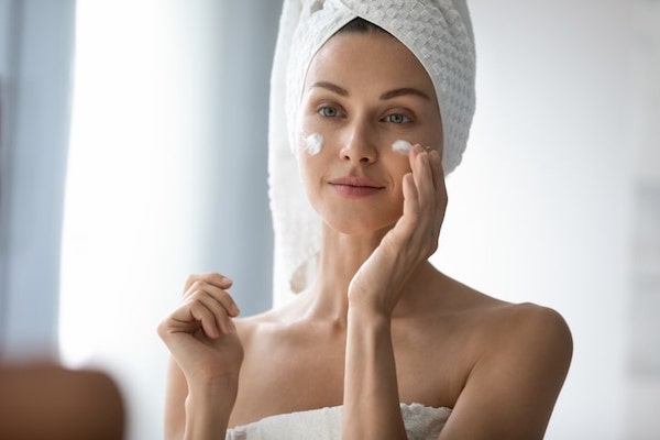 Woman in towel applying moisturizer in front of mirror